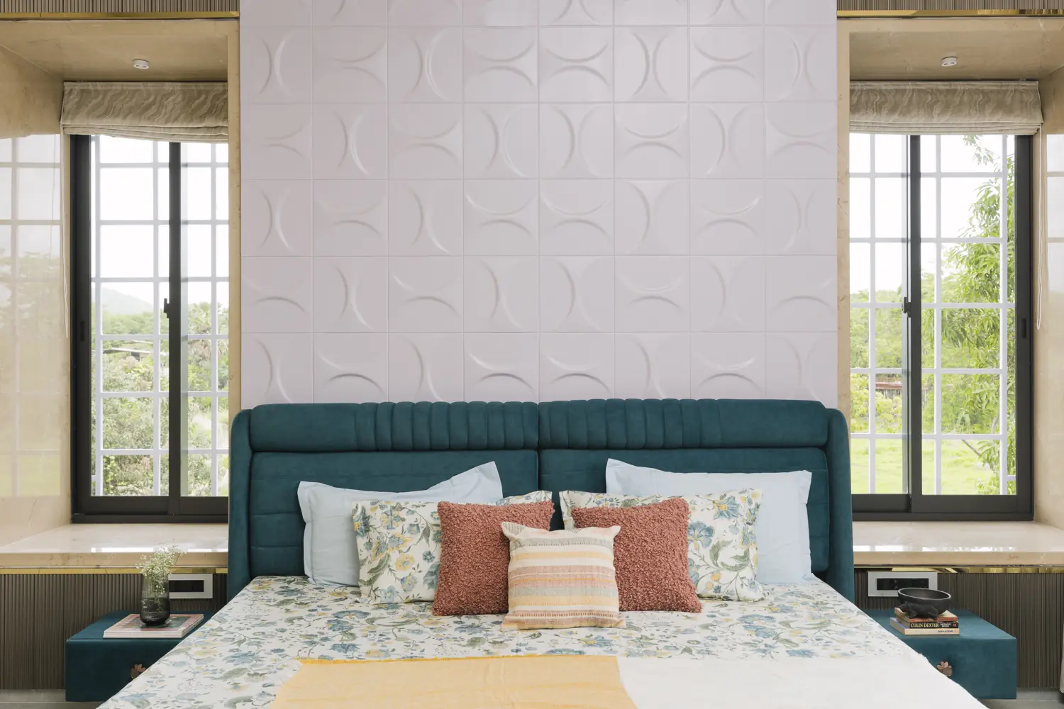 Teal bed against a white relief wall between two windows